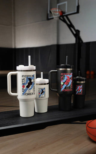 Stanley 1913 tumblers in white and black with "Everyone Watches Women's Sports" graphic, displayed on a basketball court bench.