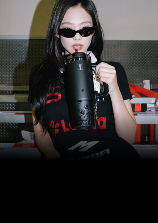 Stanley 1913 black insulated tumbler with floral charm, held by a woman in a black graphic tee and dark sunglasses.