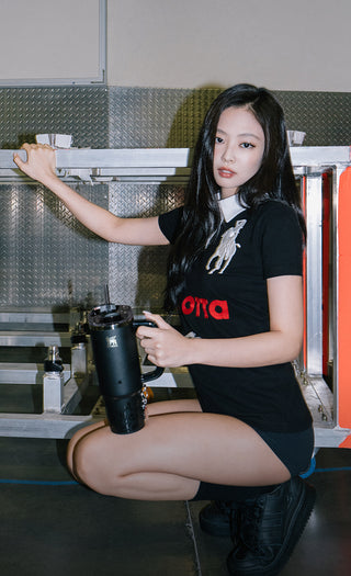 Stanley 1913 black tumbler held by a woman in an industrial setting, wearing a black graphic tee.