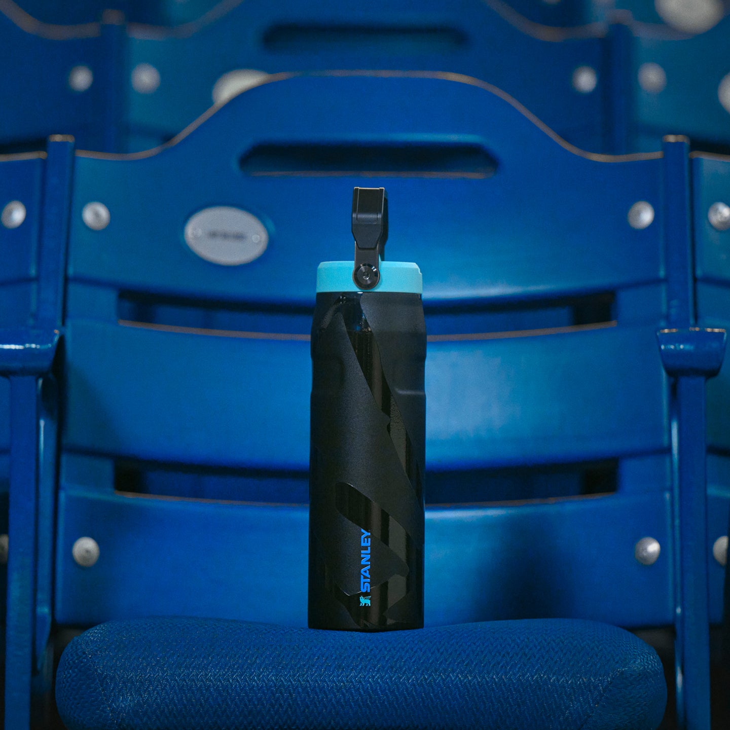 Stanley 1913 black Caitlin Clark water bottle with teal lid on a blue stadium seat