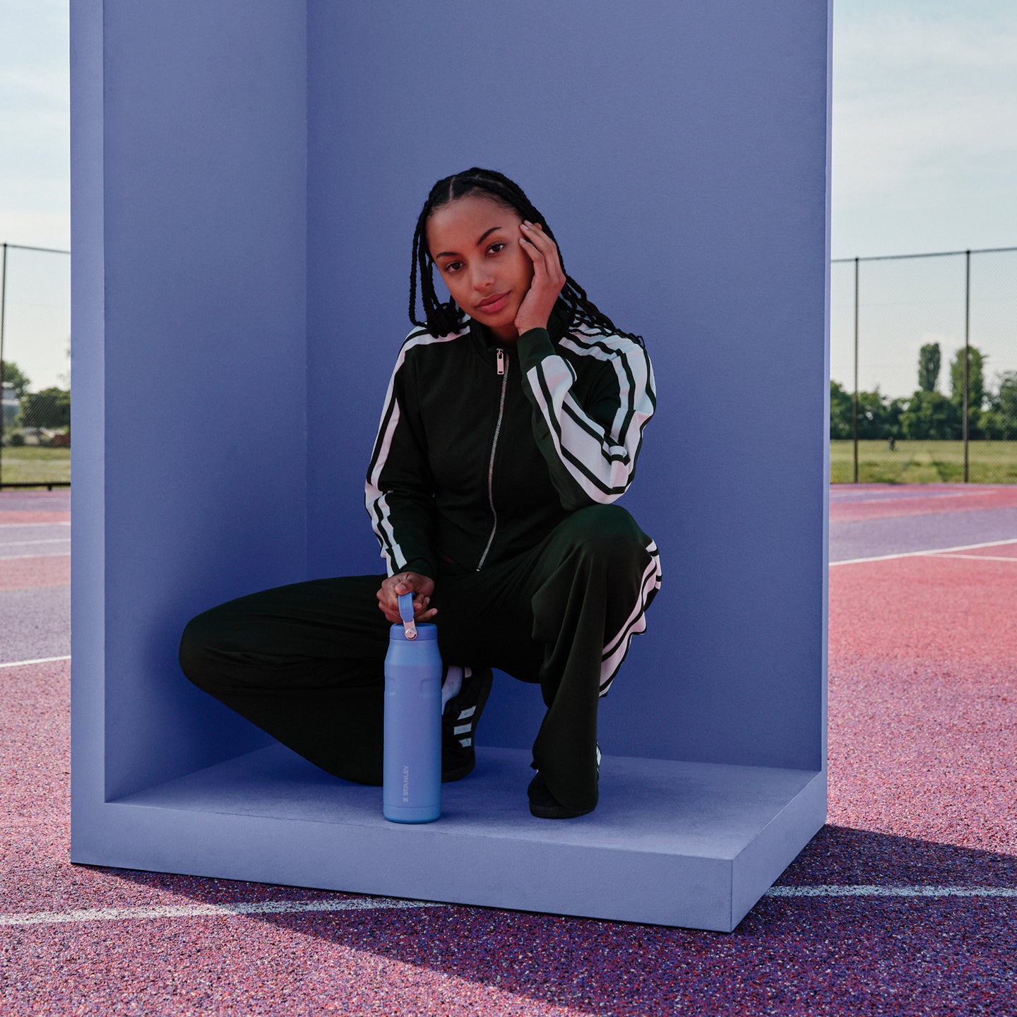 Stanley 1913 blue water bottle beside Caitlin Clark in a dark tracksuit crouching on a purple athletic court set.