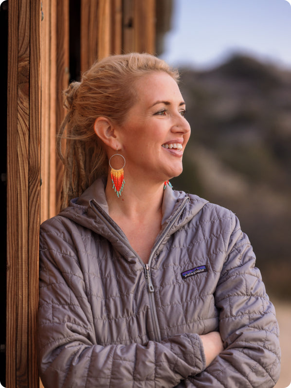 Woman in gray Patagonia jacket with colorful beaded earrings, smiling outdoors against a mountain backdrop.