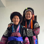Two women in traditional embroidered clothing smiling together indoors